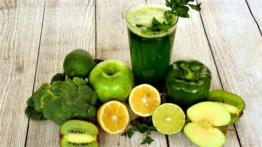Früchte und Gemüse liegen vor einem Glas mit grünem Saft.