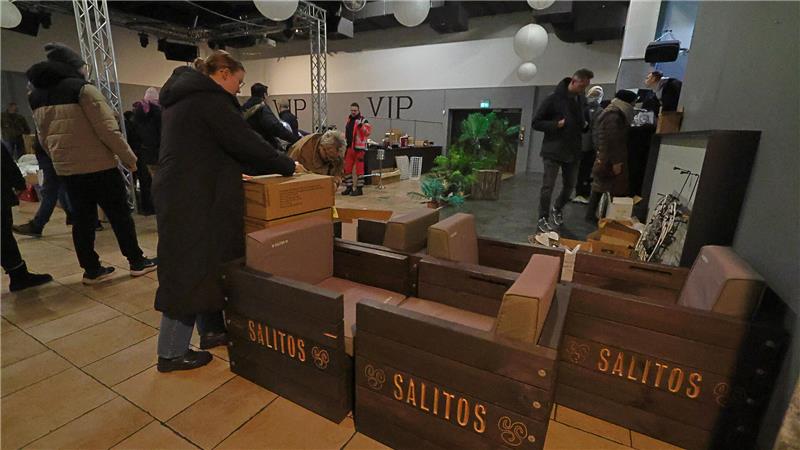 Drei Sessel mit dem Schriftzug "Salitos" stehen im Vordergrund des Bildes. Links steht eine Frau mit einem Karton in der Hand.