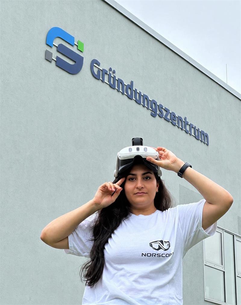 Das Foto zeigt Sara Sarvestani mit weißem T-Shirt und VR-Brille vorm Gründungszentrum in Clausthal-Zellerfeld.