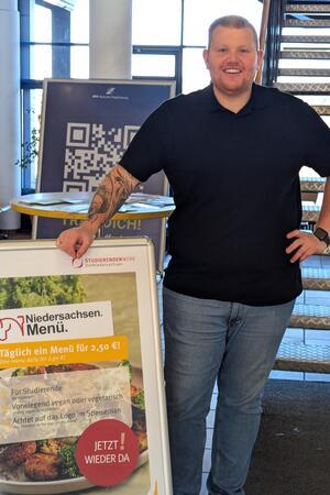 Sascha Kortegast lächelt neben einem Schild, was das Niedersachsen-Menü bewirbt.