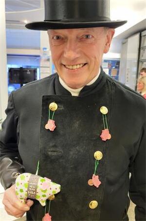 Der GZ-Schweinchenverkauf läuft in Goslar auf Hochtouren Person in schwarzer traditioneller Kleidung und Zylinder hält ein Schwein aus Stoff mit der Aufschrift 'HAPPY NEW YEAR 2026'