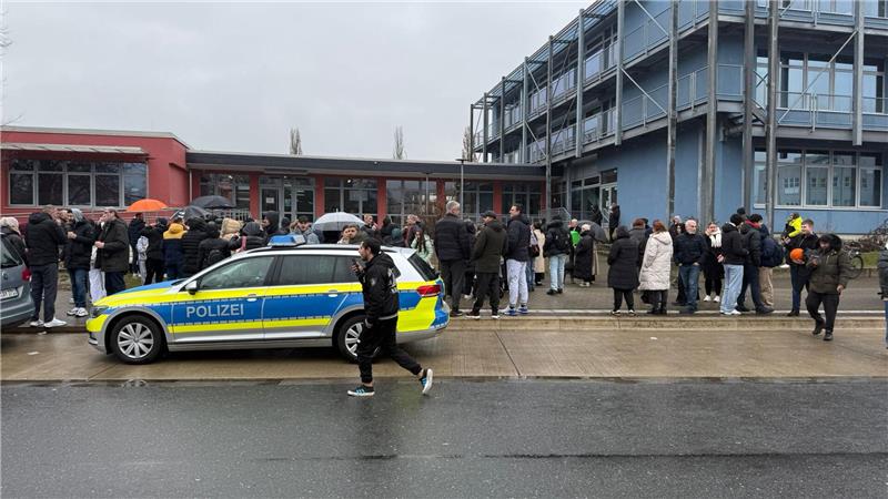 Viele Schüler und ein Polizeiauto stehen vor dem betroffenen Gebäude