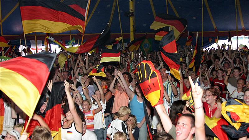 Menschenmenge in einem Zelt, die deutsche Fahnen schwenkt und jubelt