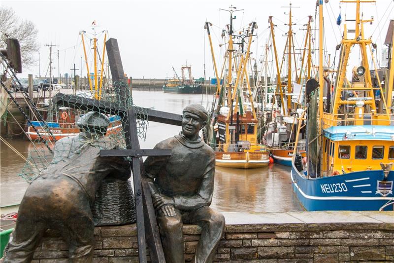 Schwarze Holzkreuze lehnen an der Bronezeskulptur «Alt- und Jungfischer» im Hafen in Neuharlingersiel. Das Fischen mit Grundschleppnetzen steht in der Kritik.
