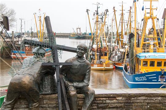 Schwarze Holzkreuze lehnen an der Bronezeskulptur «Alt- und Jungfischer» im Hafen in Neuharlingersiel. Das Fischen mit Grundschleppnetzen steht in der Kritik.
