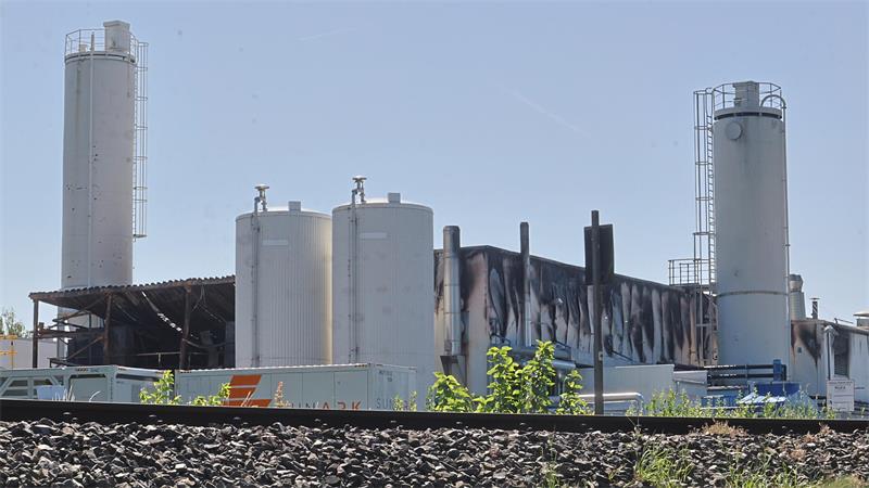 Industrieanlage mit mehreren hohen zylindrischen Tanks und einem Gebäude mit dunklen Verfärbungen an der Fassade im Hintergrund.