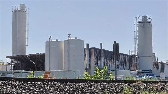 Industrieanlage mit mehreren hohen zylindrischen Tanks und einem Gebäude mit dunklen Verfärbungen an der Fassade im Hintergrund.