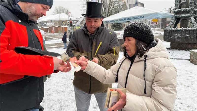 Zwei Männer verkaufen einer Frau im verschneiten Braunlage Glücksschweinchen.