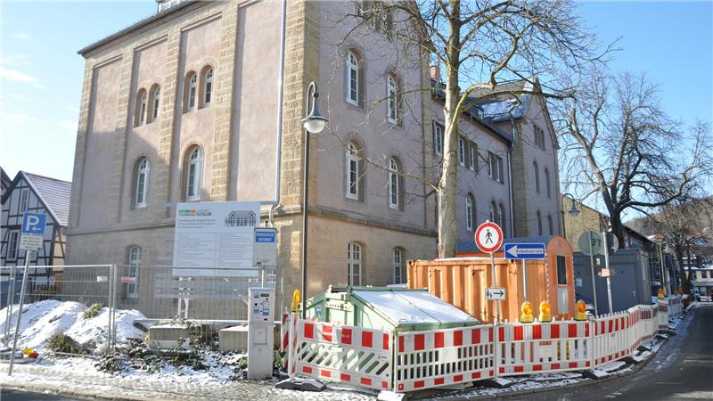 Altbau mit Baustelleneinzäunung und Containern an einer schneebedeckten Straße