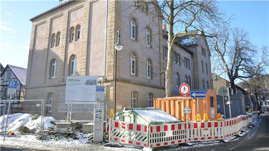 Altbau mit Baustelleneinzäunung und Containern an einer schneebedeckten Straße