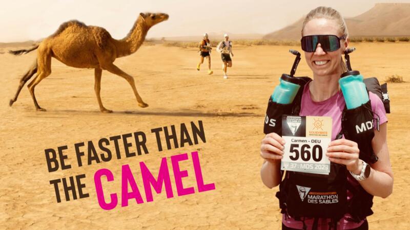 Frau posiert in der Wüste für ein Foto, im Hintergrund läuft ein Kamel 