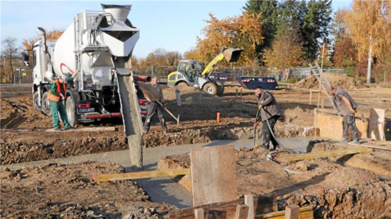 Arbeiter schütten mit Hilfe eines Betonmischers Zement in den Boden.