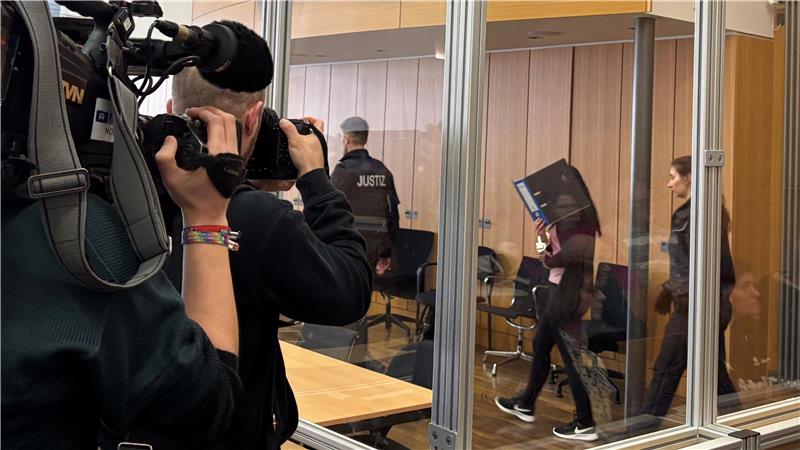 Kameramann filmt durch eine Glaswand in einen Raum, in dem mehrere Personen, darunter Polizisten, gehen.