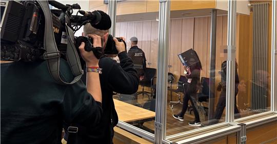 Kameramann filmt durch eine Glaswand in einen Raum, in dem mehrere Personen, darunter Polizisten, gehen.