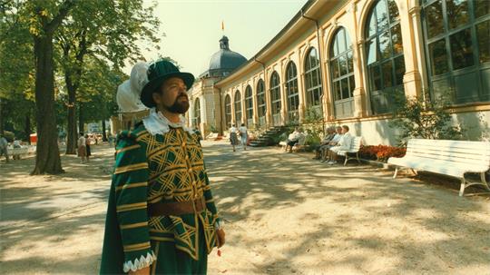 Ein Mann in einem historischen Kostüm schaut auf ein ebenso historisches Gebäude.