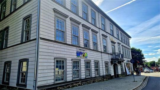 Historisches Rathaus in Clausthal-Zellerfeld mit vielen Fenstern und einem kleinen Balkon über einem Torbogen an einer gepflasterten Straße.