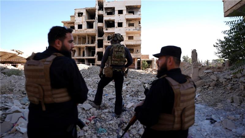 Sicherheitskräfte aus Syrien und aus Deutschland sichern den Besuch von Außenminister Wadephul bei einem humanitären Projekt in einer Straße mit während des Bürgerkriegs zerbombten Häusern in Harasta ab. 