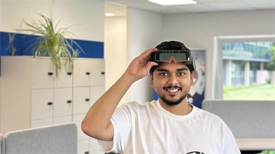 Das Foto zeigt Siddhant Rebello mit weißem T-Shirt und VR-Brille über den Augen in einem Raum der TU Clausthal.