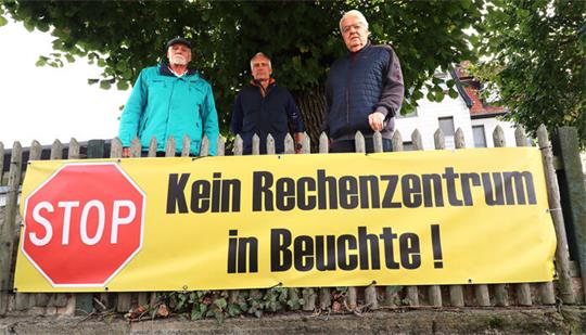 Drei Männer stehen hinter einem Zaun mit Protestplakat.