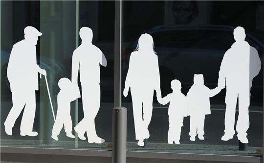 Silhouetten von Menschen in verschiedenem Alter sind auf Fensterscheiben aufgeklebt.