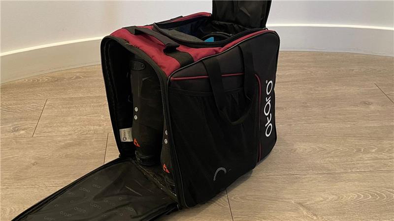 Schwarze und dunkelrote Tasche mit geöffnetem Hauptfach und aufklappbarer Frontseite auf hellem Holzboden.