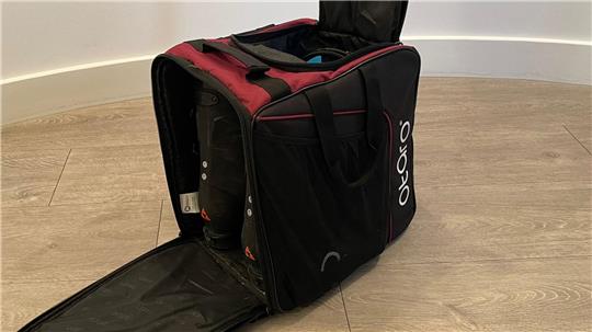 Schwarze und dunkelrote Tasche mit geöffnetem Hauptfach und aufklappbarer Frontseite auf hellem Holzboden.