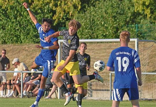 Mehrere Fußballspieler kämpfen um den Ball in der Luft auf einem Spielfeld mit Zuschauern im Hintergrund.