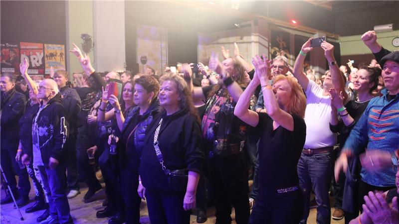 Gruppe von Menschen in einem Innenraum, die mit erhobenen Armen und Händen an einem Event teilnehmen.