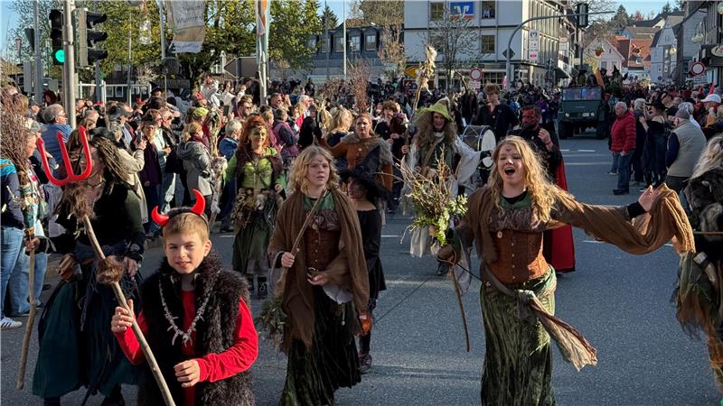 Das Foto zeigt Hexen und Teufel, die vor vielen Zuschauern auf der Straße marschieren.