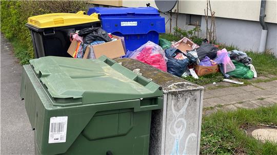 Mehrere Mülltonnen vor einem Haus mit einem Haufen Müllsäcken und Kartons auf dem Gehweg