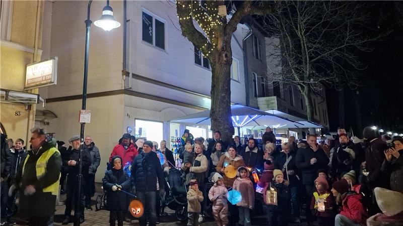 Menschen stehen mit Laternen vor Häusern.