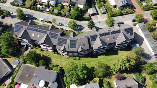 Luftaufnahme eines Wohnhauses mit mehreren Dächern, die mit Solarpaneelen bedeckt sind, umgeben von Bäumen und weiteren Gebäuden