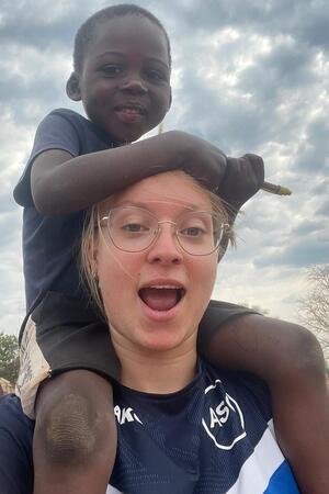 Goslarerin Amalia Saupe trainiert Mädchenteam in Afrika (Teil 2) Kind sitzt auf den Schultern einer Person vor bewölktem Himmel.