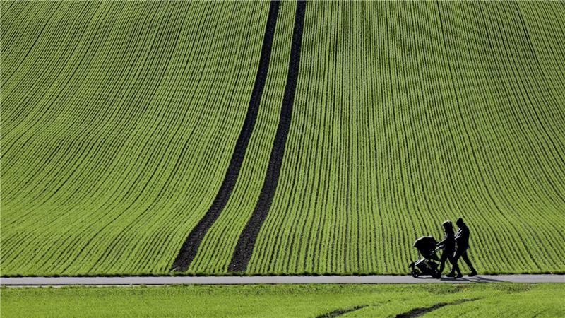 Spaziergänger gehen im Sonnenschein an einem frisch bestellten Feld in Baden-Württemberg vorbei.