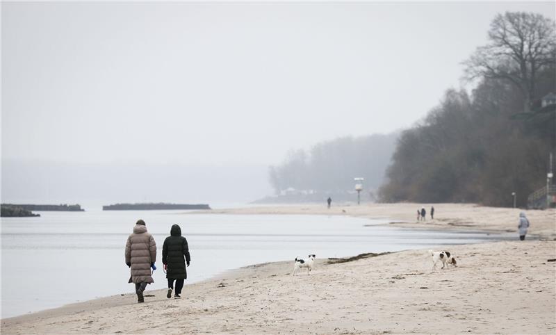 Spaziergänger mit Hunden sind bei leichtem Nieselregen am Strand von Schilksee bei Kiel.