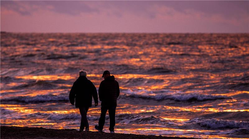 Spaziergänger sind nach Sonnenuntergang am Strand von Warnemünde an der Ostsee unterwegs.