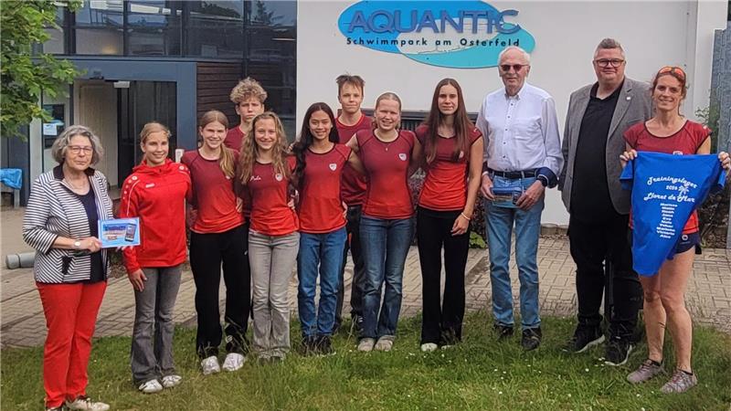 Gruppe von elf Personen vor einem Gebäude mit dem Schriftzug 'AQUANTIC Schwimmsport am Osterfeld', einige tragen rote Shirts, eine Person hält ein blaues T-Shirt mit weißem Aufdruck