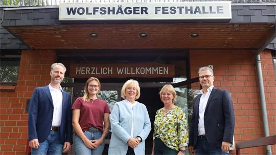 Fünf Personen stehen vor dem Eingang der Wolfshäger Festhalle unter einem Schild mit der Aufschrift 'WOLFSHÄGER FESTHALLE' und einem weiteren Schild mit 'HERZLICH WILLKOMMEN'