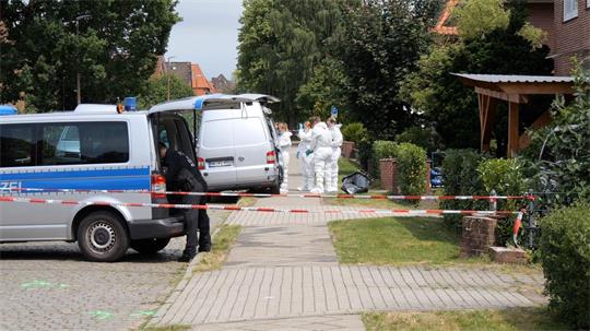 Auf dem Bild sind ein Polizeiauto und Mitarbeiter der Spurensicherung in Schutzanzügen zu sehen.