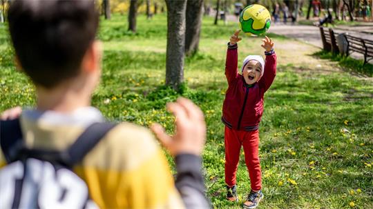 Ein Kleinkind wirft einem Schulkind einen Ball zu.