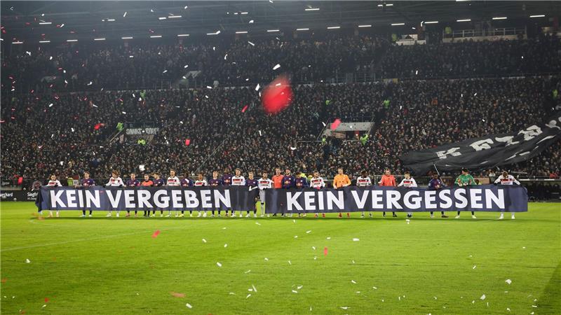 Spieler beider Teams halten vor Spielbeginn ein Banner anlässlich das Holocaust-Gedenktags hoch.