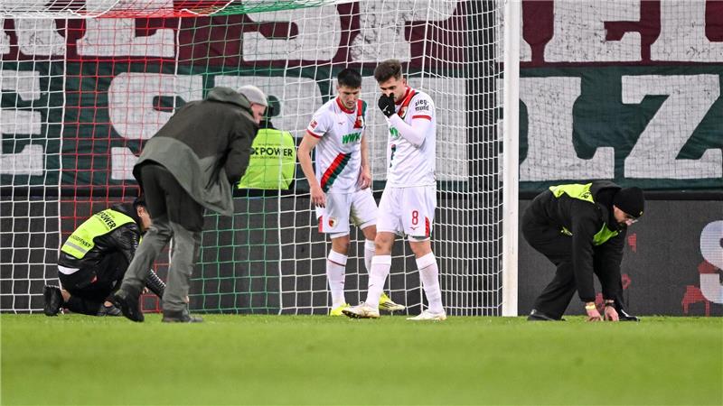 Spieler und Ordner sammeln nach dem Fanprotest Gegenstände vom Rasen.