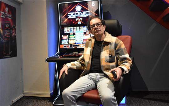 Person sitzt in einem Sessel vor einem Spielautomaten mit der Aufschrift 'ZONIC FIVE'.