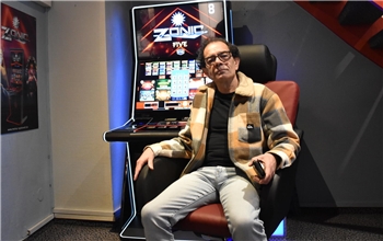 Person sitzt in einem Sessel vor einem Spielautomaten mit der Aufschrift 'ZONIC FIVE'.