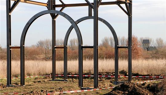Stahlkonstruktionen symbolisieren auf dem Pfalzgelände die Tore der Vorburgen – im Hintergrund das rekonstruierte Werla-Westtor der Kernburg.