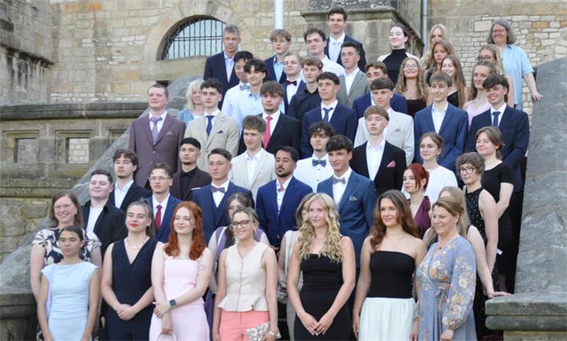 Gruppenfoto von jungen Erwachsenen in formeller Kleidung auf einer Steintreppe vor einem historischen Gebäude