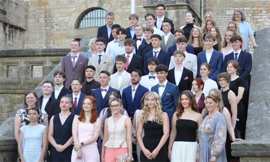 Gruppenfoto von jungen Erwachsenen in formeller Kleidung auf einer Steintreppe vor einem historischen Gebäude
