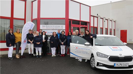 Gruppe von Frauen vor einem Gebäude mit roten Fensterrahmen neben einem weißen Auto mit Aufschrift.