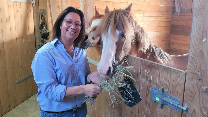 Eine Frau steht im Stall und füttert ein Pferd mit Heu.