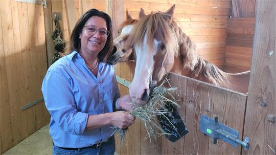 Eine Frau steht im Stall und füttert ein Pferd mit Heu.